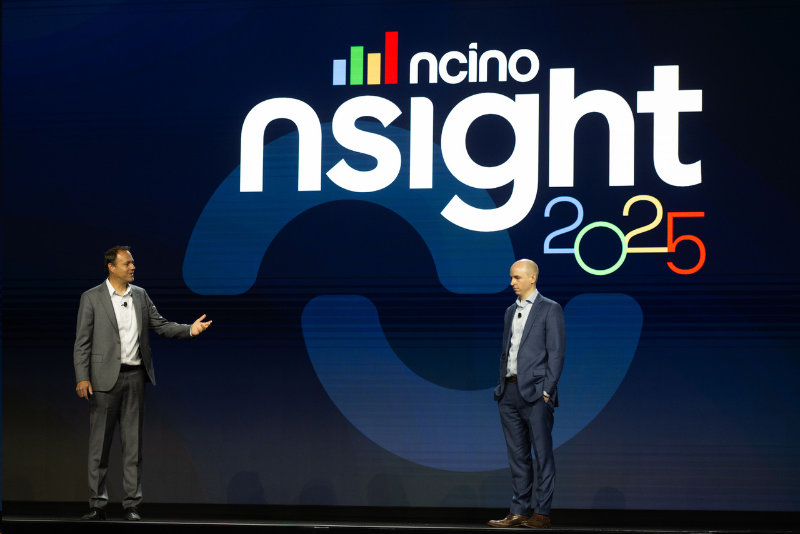 Two individuals in business attire stand on a stage in front of a large screen displaying the text "nCino nSight 2025"